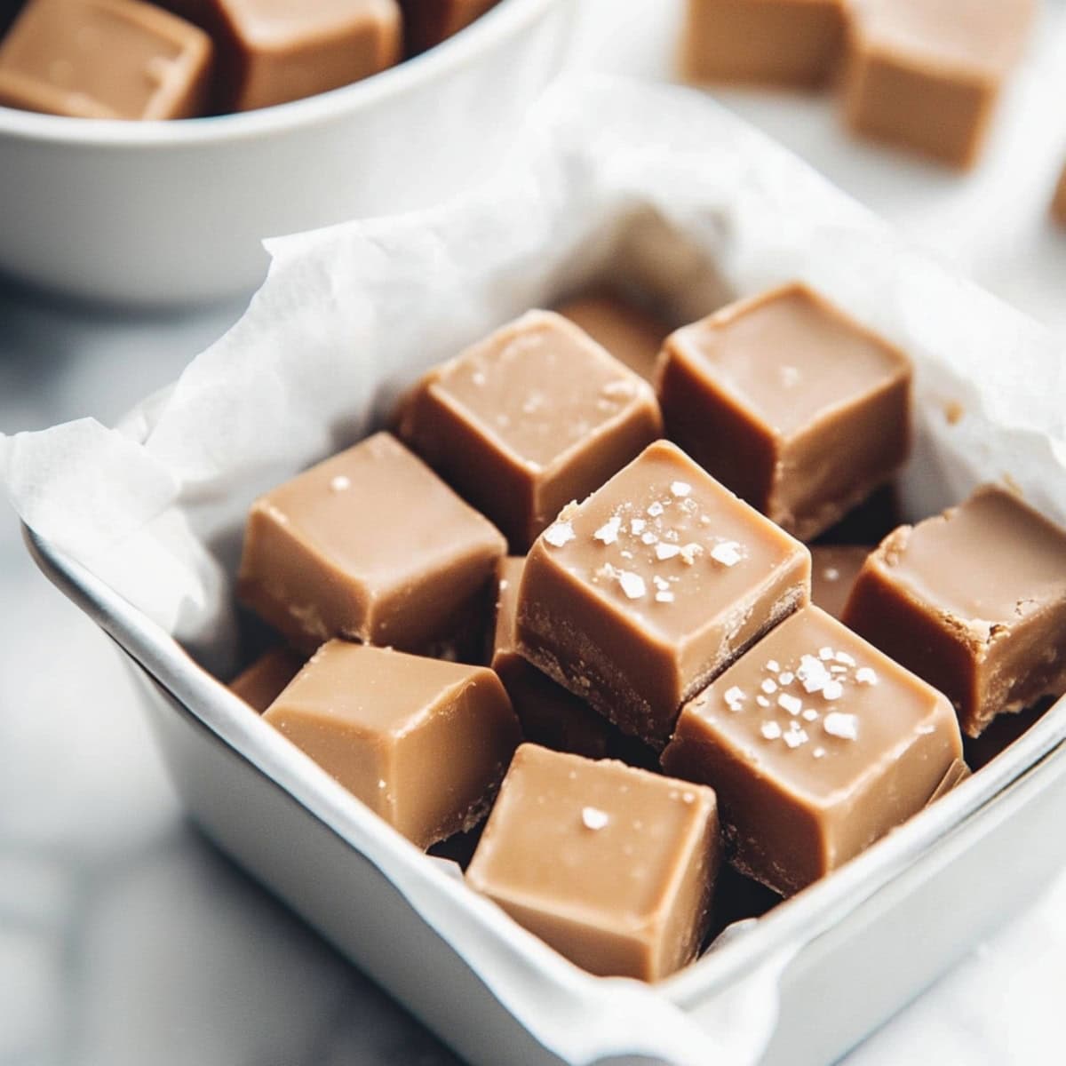 Salted caramel fudge squares in a square pan with parchment paper sitting on a marble table top view.