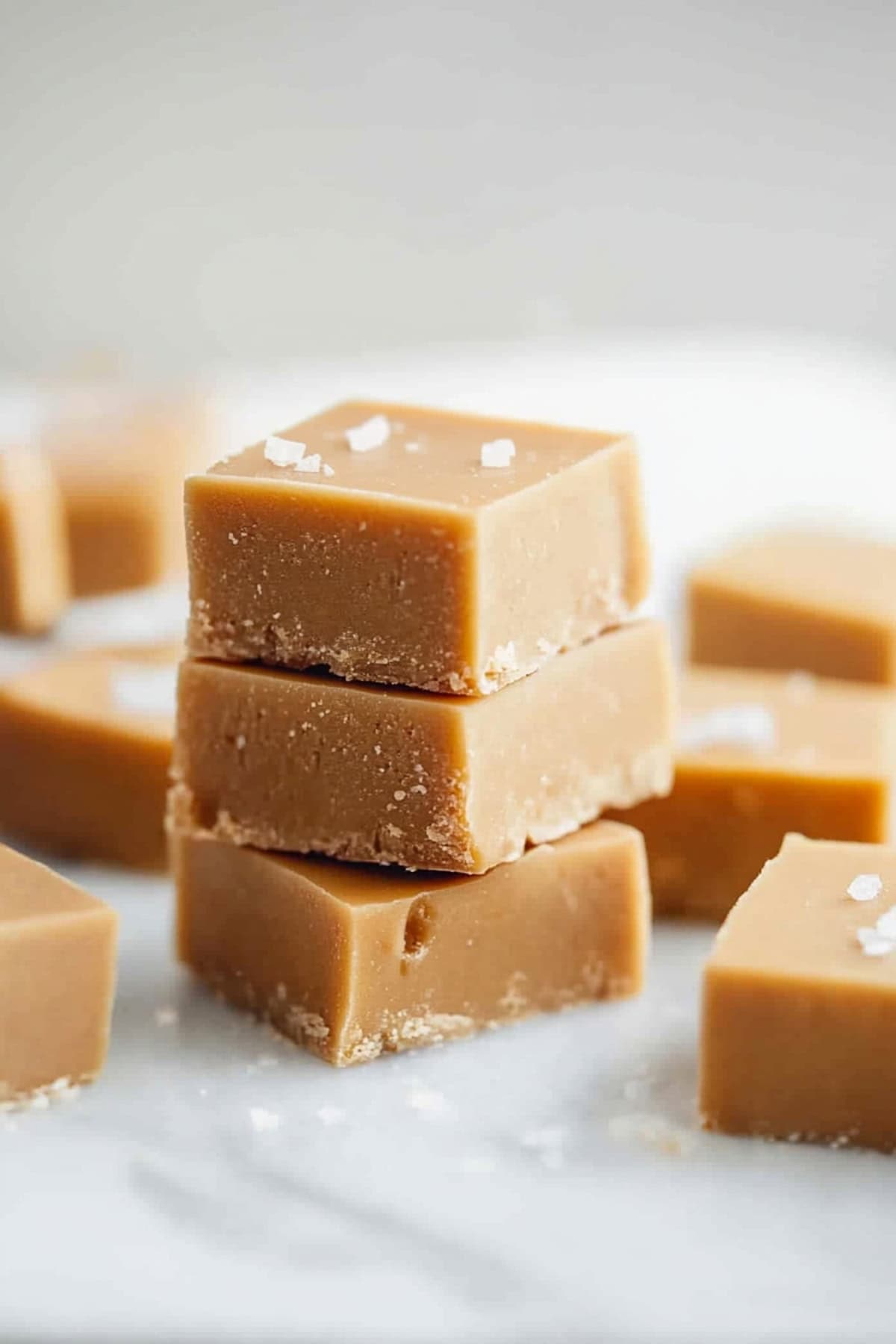 Square slices of caramel fudge stacked on top of each other on a marble table, side view