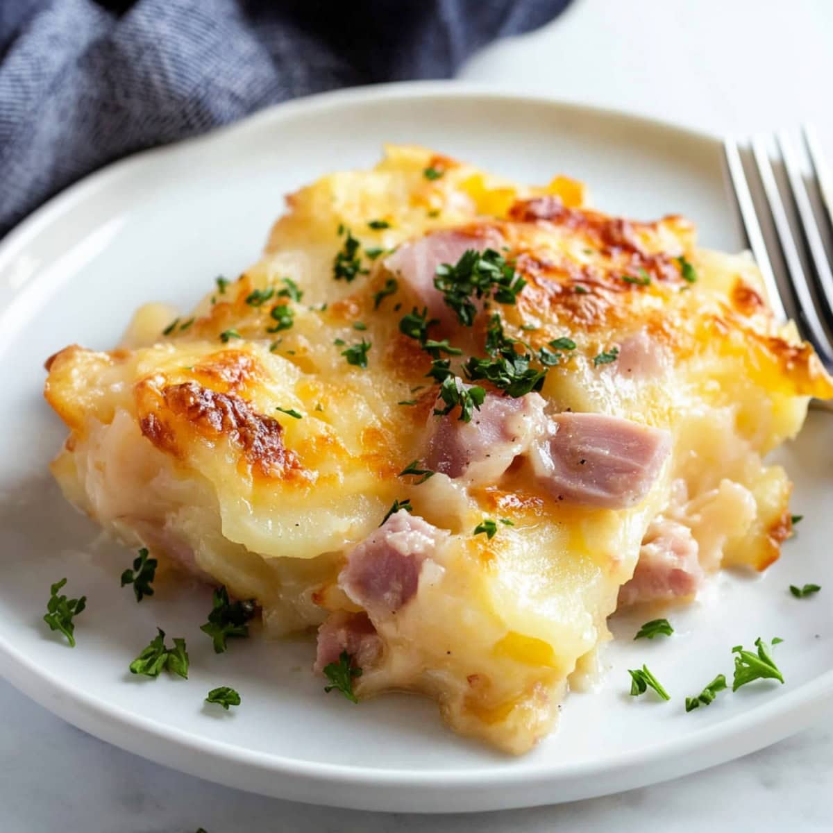 A serving of scalloped potatoes and ham with a crispy, cheesy crust, displayed in a white plate.