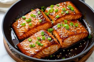 Salmon slices cooked in teriyaki sauce in a skillet pan.