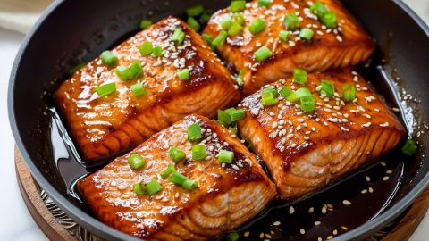 Salmon slices cooked in teriyaki sauce in a skillet pan.