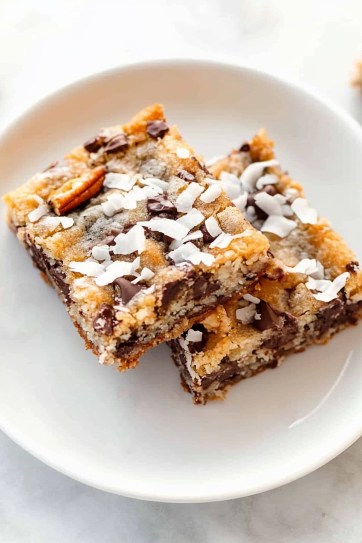 Magic cookie bars on a white plate, showing layers of condensed milk, chocolate, and shredded coconut.