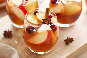 Three glasses of apple cider sangria serving sitting on top of wooden board.