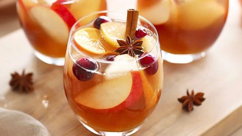 Three glasses of apple cider sangria serving sitting on top of wooden board.