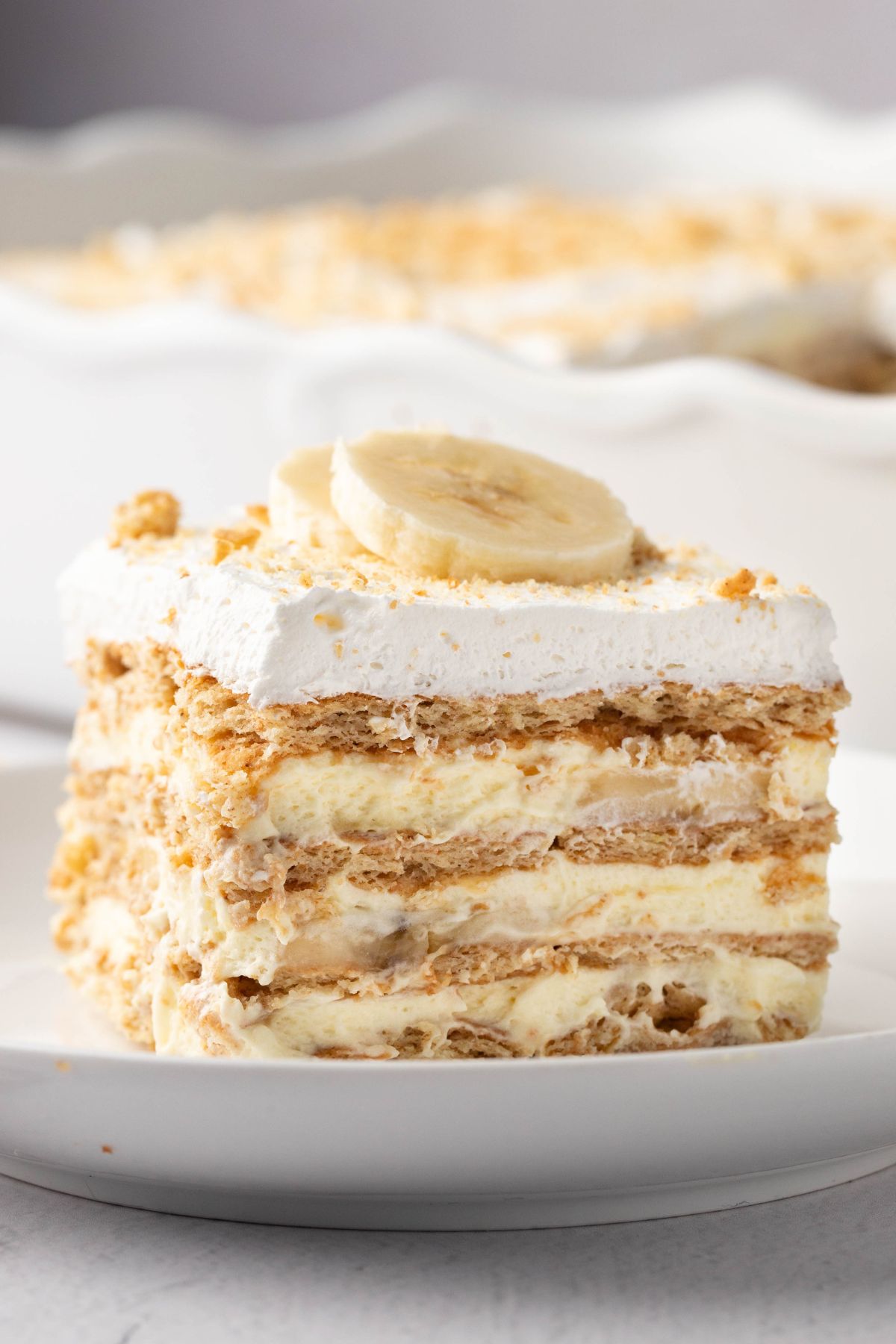  A slice of banana icebox cake served in a white plate garnished with a slice of banana on top.
