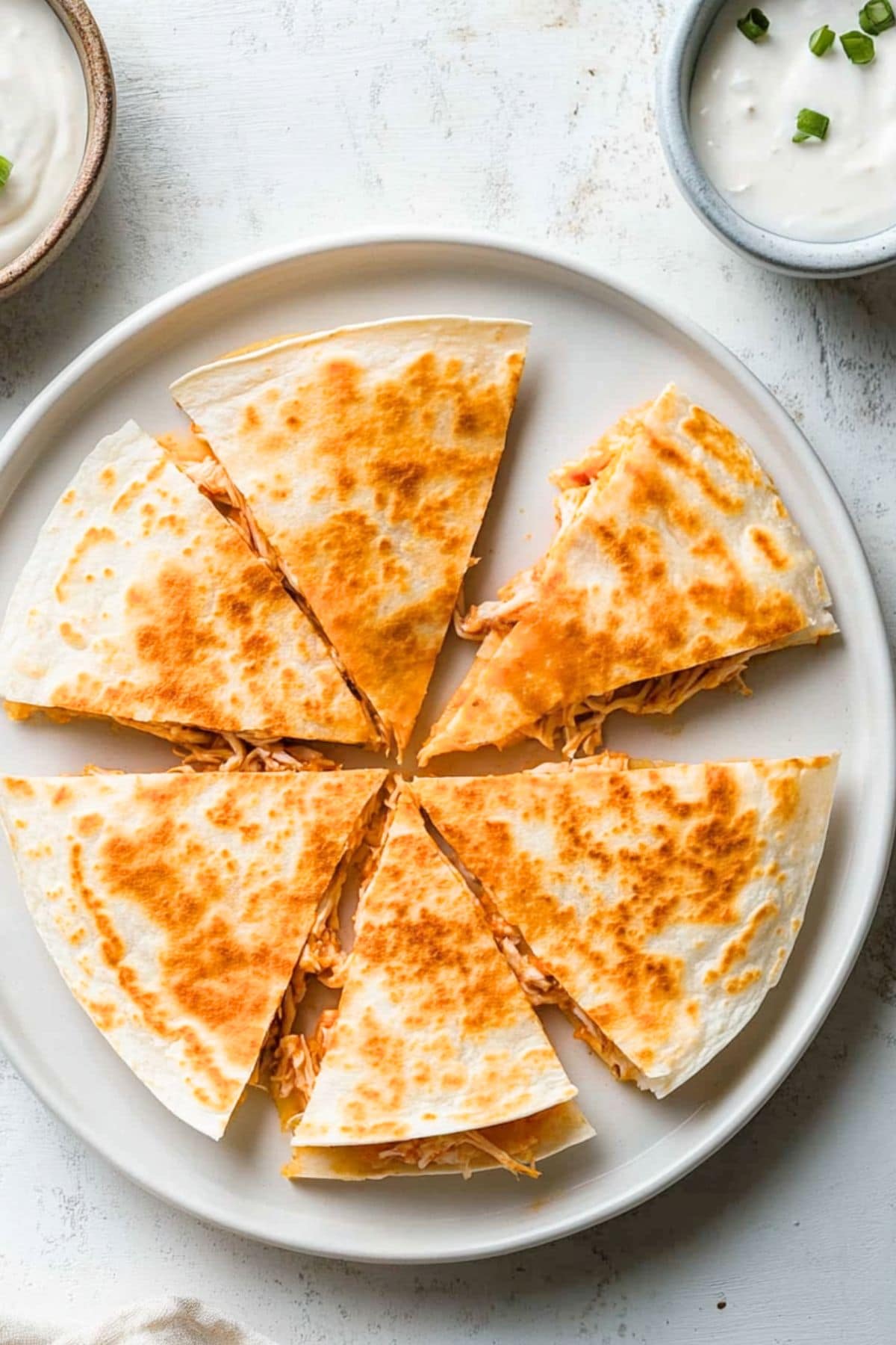 Sliced quesadilla filled with shredded buffalo flavored chicken arranged in a plate.