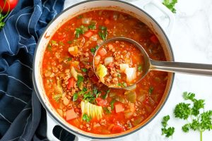 Cabbage roll soup serving lifted by a metal ladle from pot.