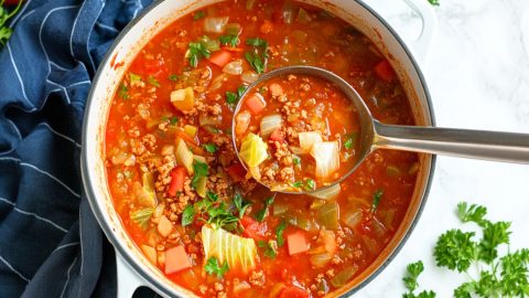 Cabbage roll soup serving lifted by a metal ladle from pot.