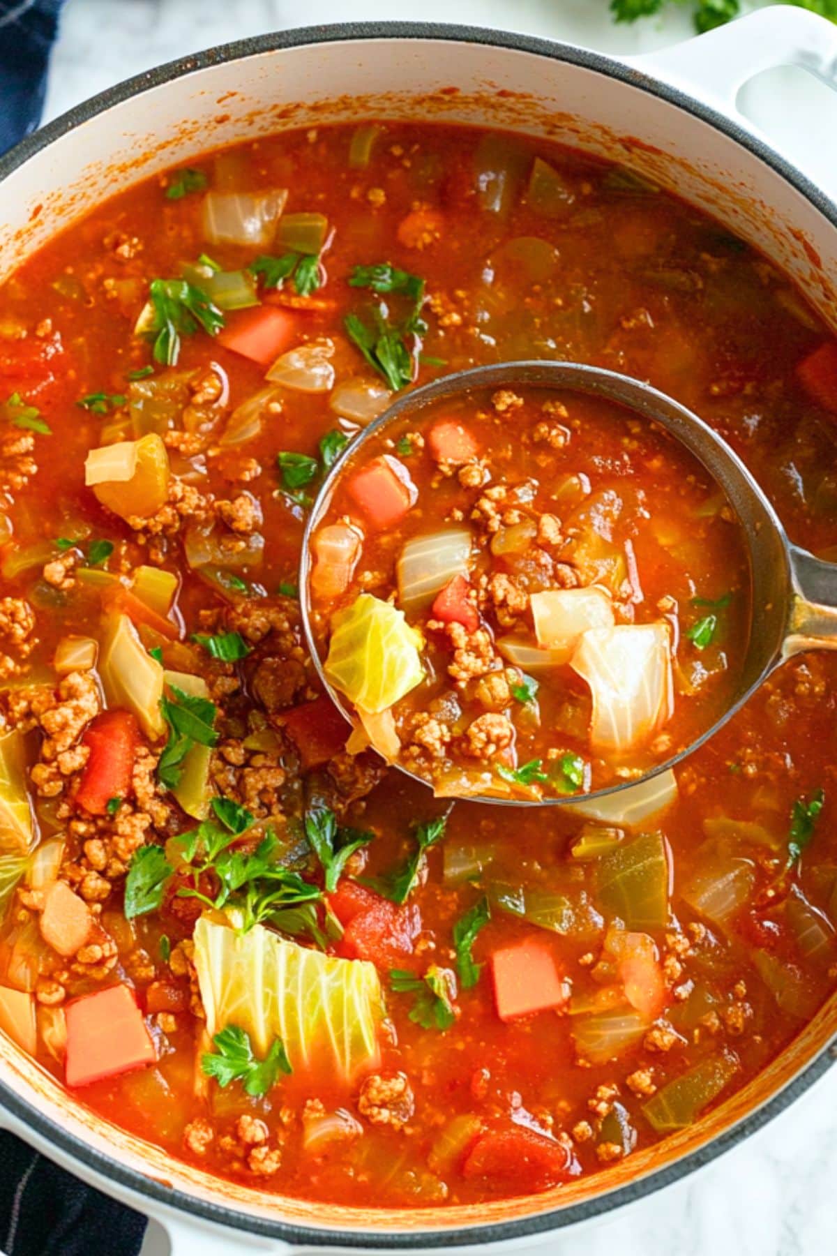 Metal soup ladle lifting a serving of tomato based cabbage roll soup from pot.