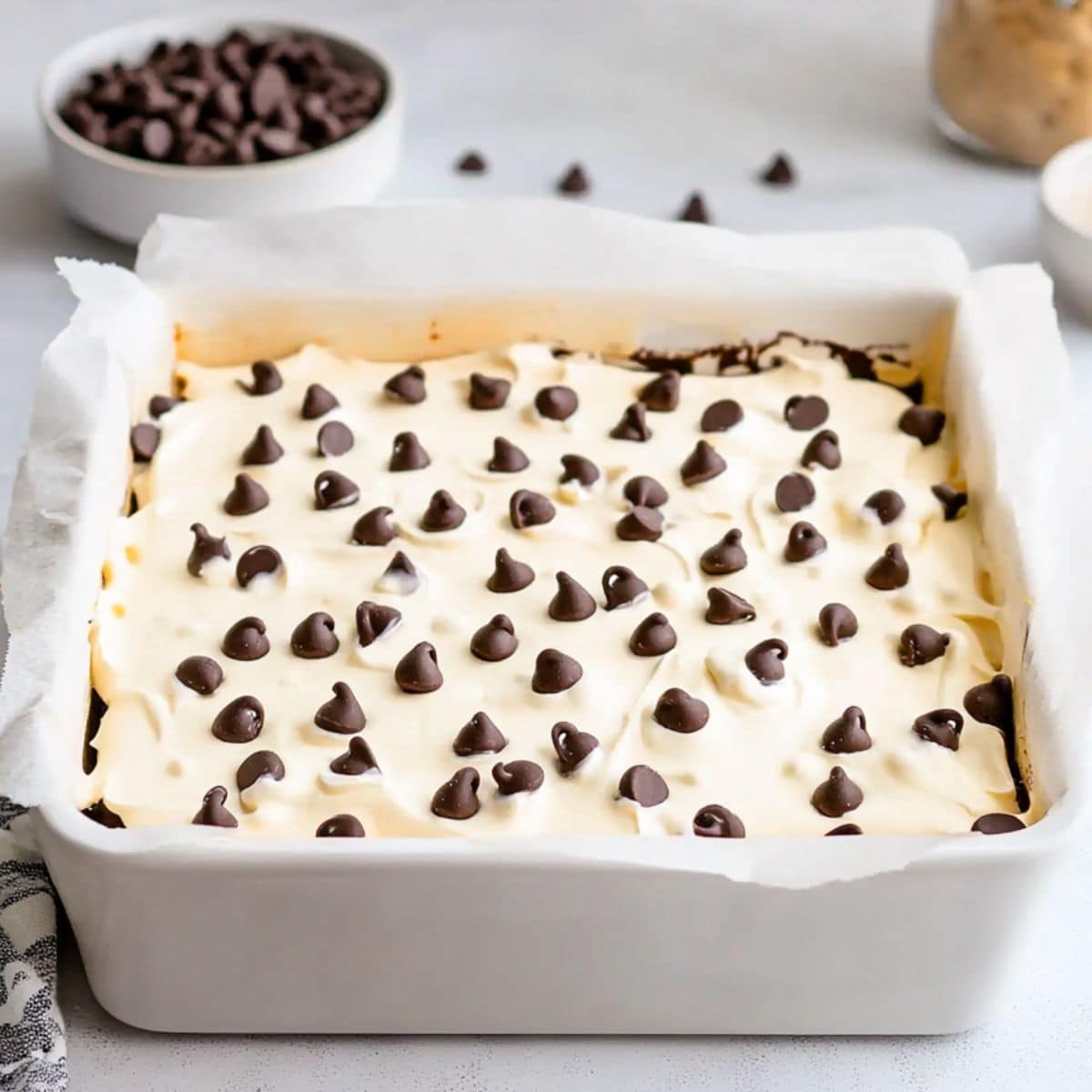 Cannoli cheesecake in a white baking dish with parchment paper hanging on sides.