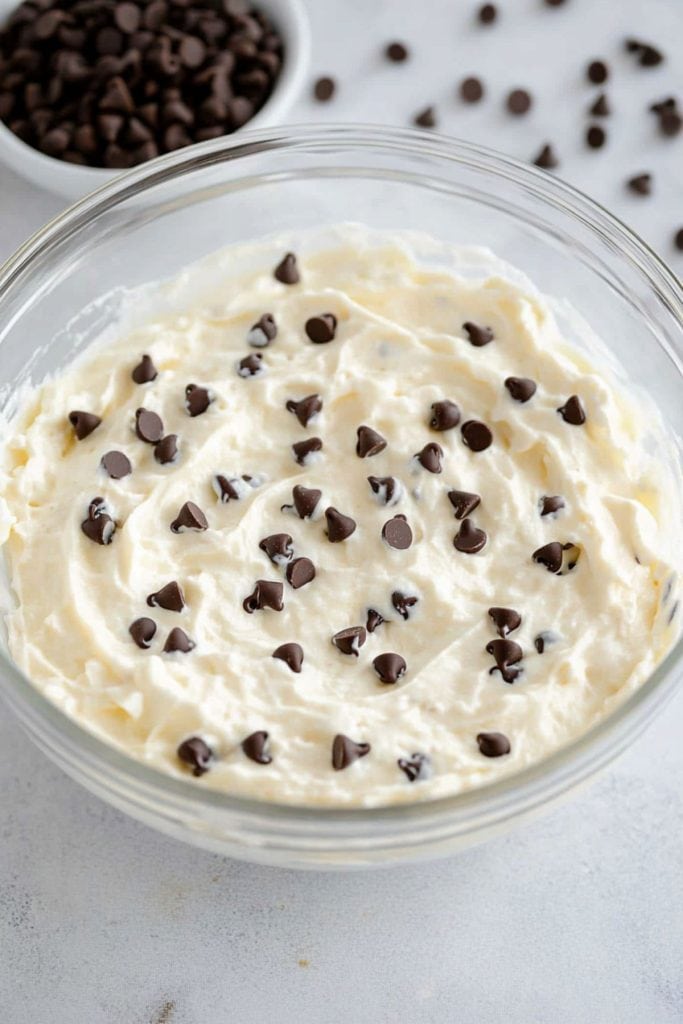 Cheesecake mixture with mini chocolate chips in a glass mixing bowl.