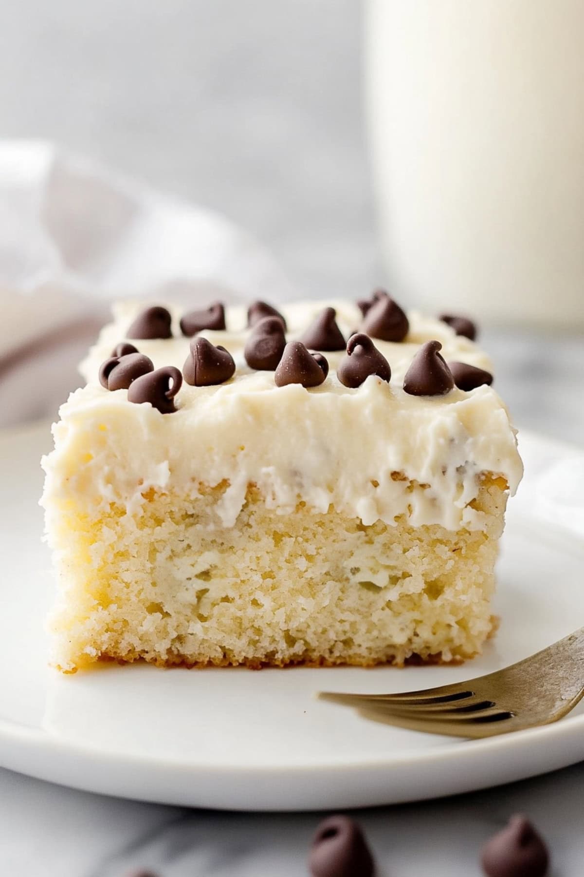 Close-up of a cannoli cake slice, showing layers of vanilla cake, creamy ricotta filling, and crunchy chocolate chips.