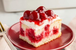 Cherry poke cake square slice served in a red plate.