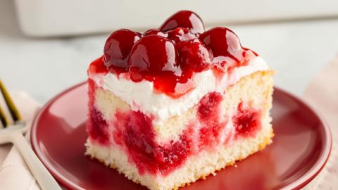 Cherry poke cake square slice served in a red plate.