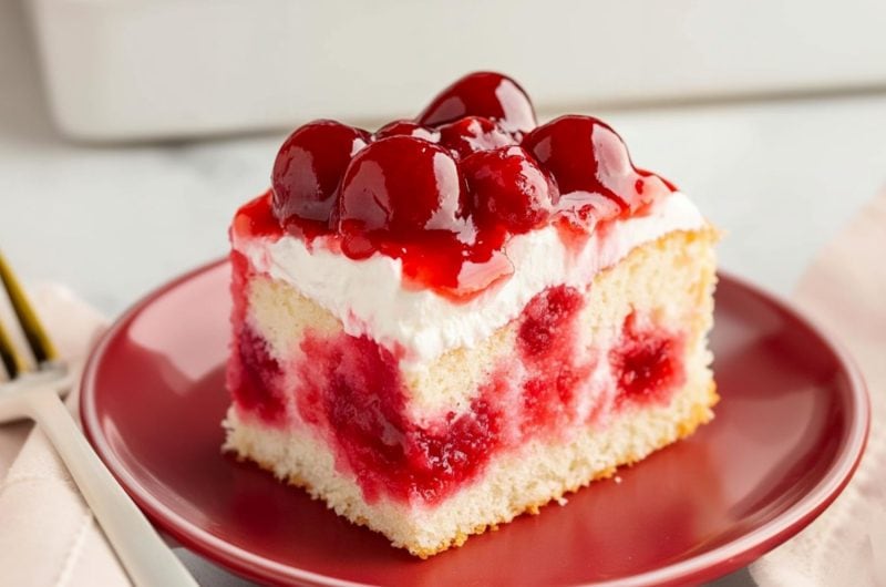 Cherry poke cake square slice served in a red plate.