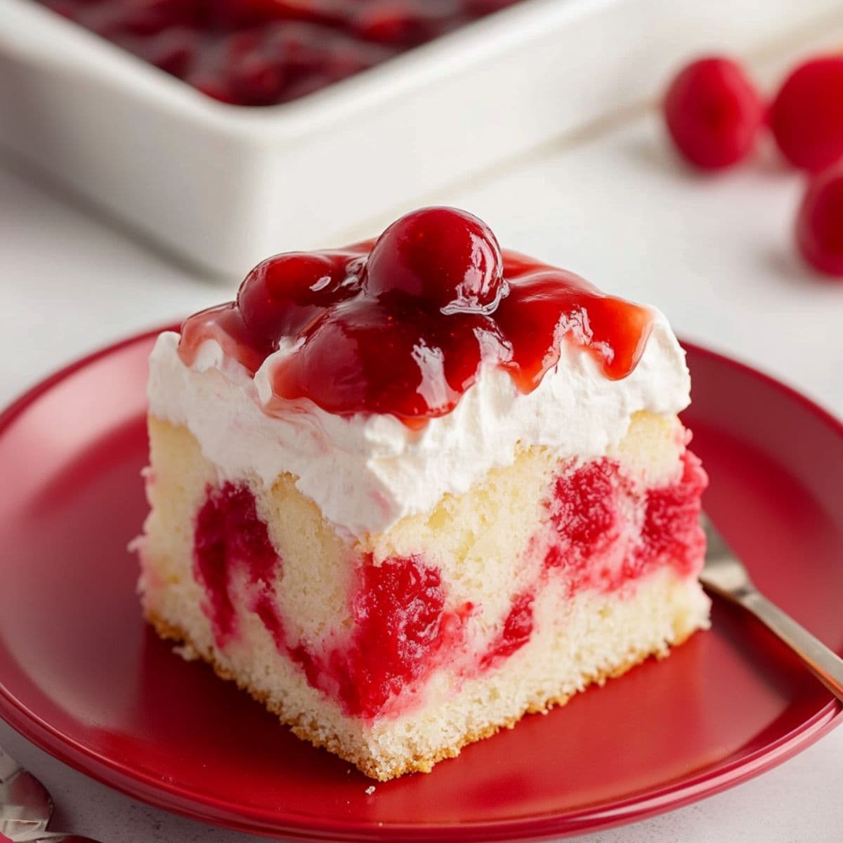 Square slice of cherry poke cake served in a red plate.