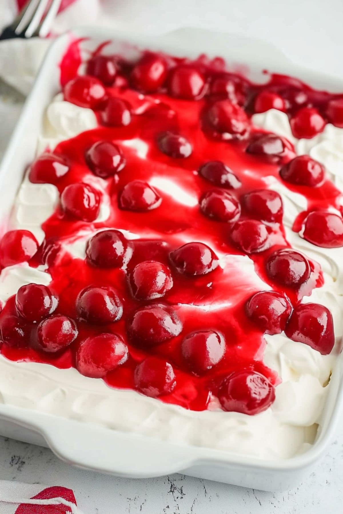 Cake in a baking dish covered with whipped cream and cherry pie filling.