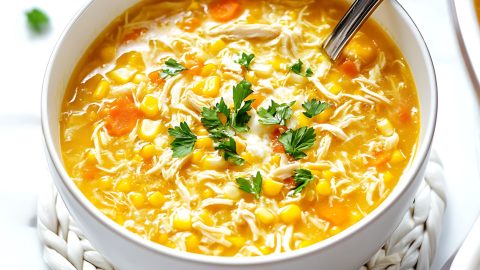 Chicken and sweet corn soup with corn kernels and carrots served in a white bowl.