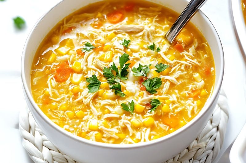 Chicken and sweet corn soup with corn kernels and carrots served in a white bowl.