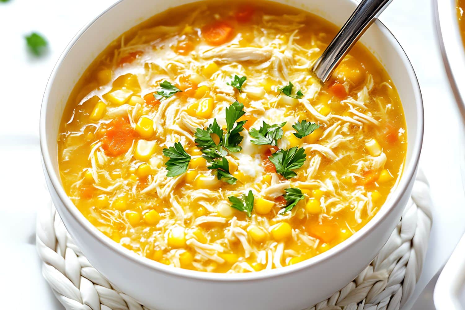 Chicken and sweet corn soup with corn kernels and carrots served in a white bowl.