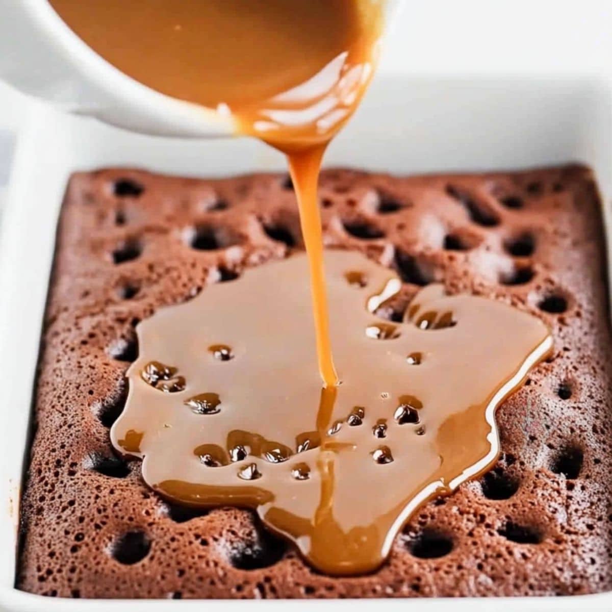 Caramel sauce drizzled over chocolate poke cake in a rectangular baking dish.