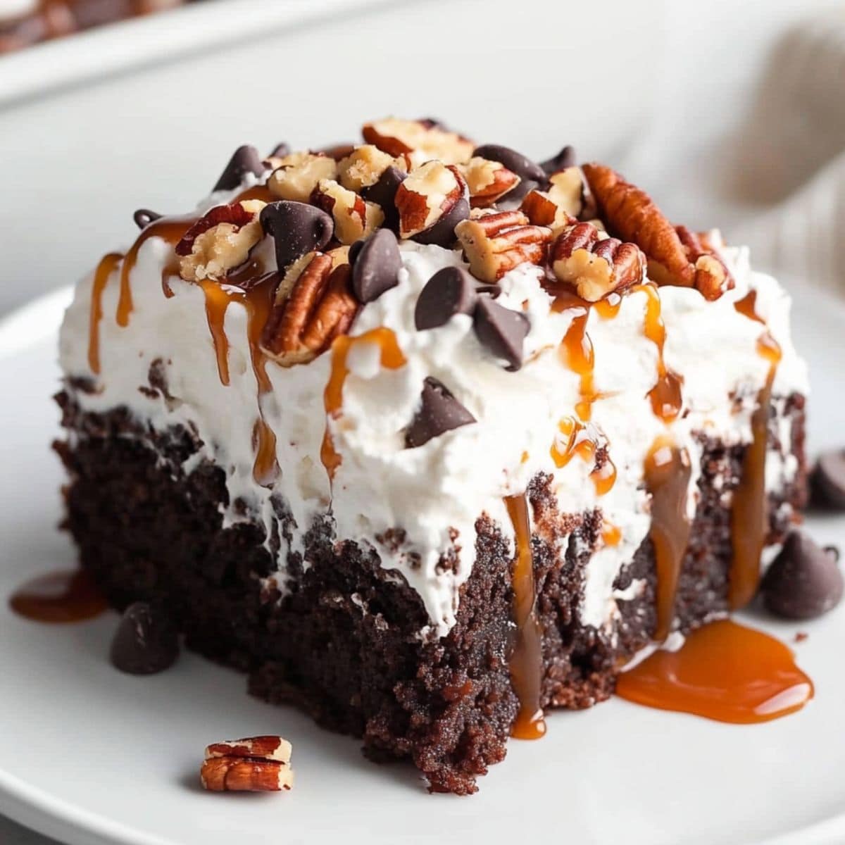 A slice of chocolate turtle poke cake drizzled with caramel on a plate