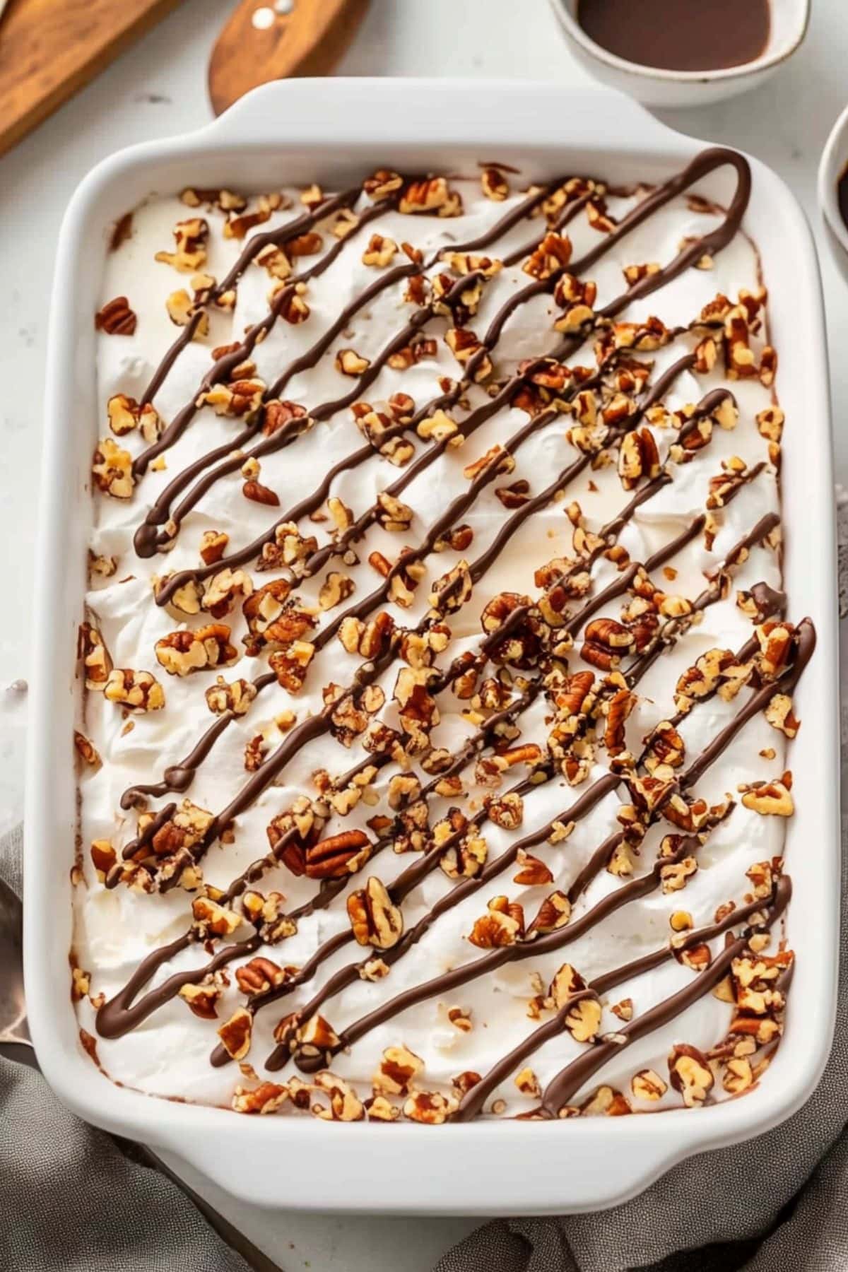 Chocolate turtle poke cake in a baking dish garnished with chopped pecans, drizzled with chocolate and caramel syrup on top.