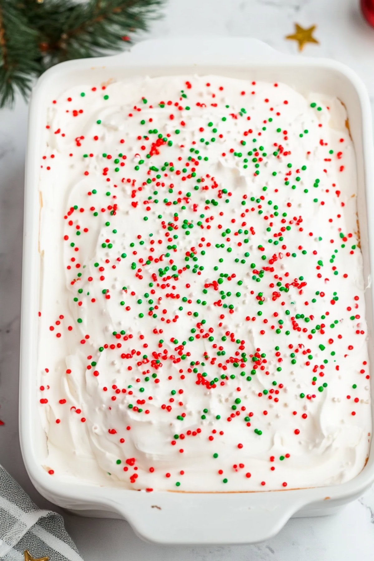 Whipped cream covered cake in a baking dish garnished with candy sprinkles on top.