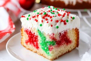 Red and green jello infused poke cake with a layer of whipped cream on top.