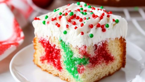 Red and green jello infused poke cake with a layer of whipped cream on top.