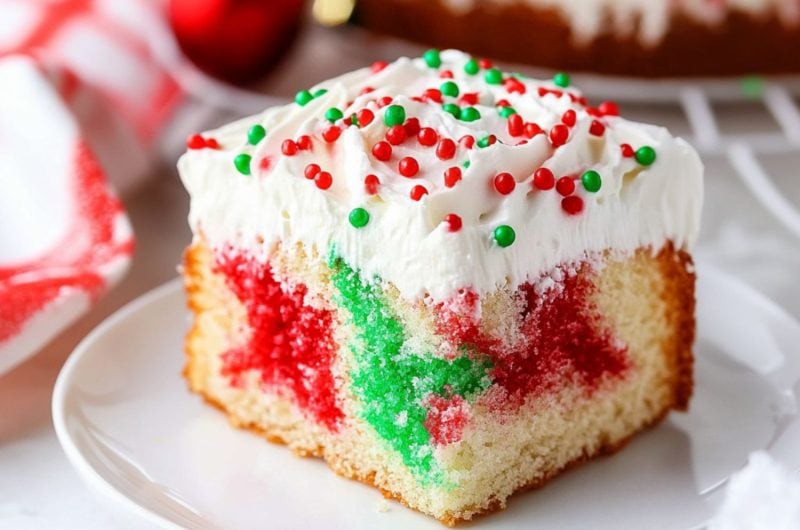 Red and green jello infused poke cake with a layer of whipped cream on top.