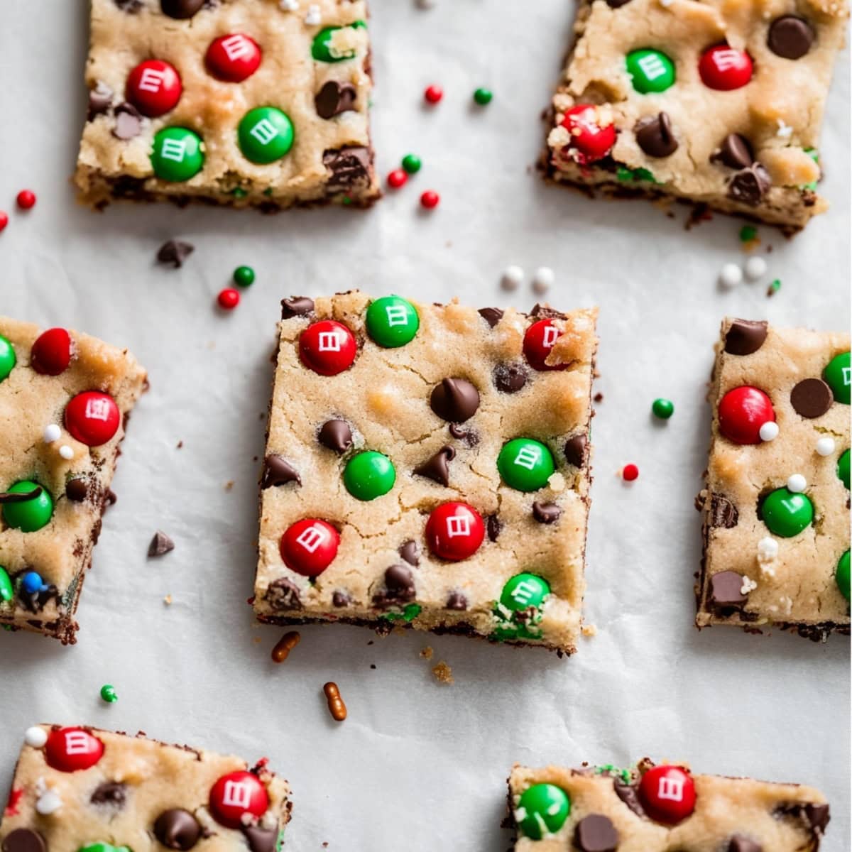 An overhead view of Christmas cookie bars with M&M cookies, chocolate chips and candy sprinkles.