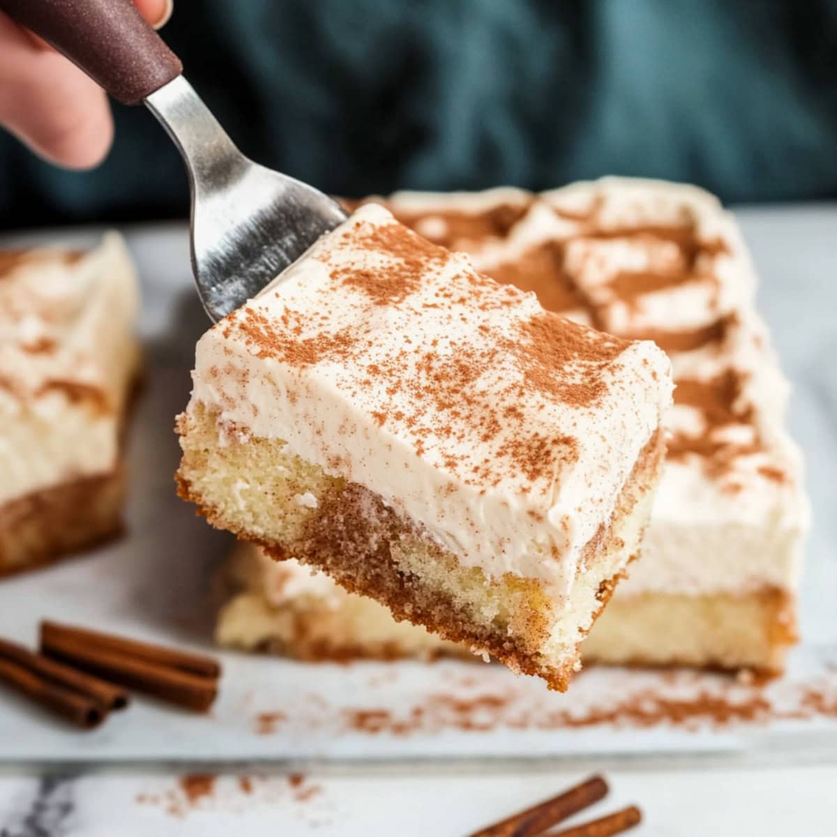 Close-up of a slice of poke cake with cream cheese frosting and cinnamon topping.