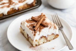 A plate of cinnamon roll poke cake with cream cheese frosting and milk on the side.