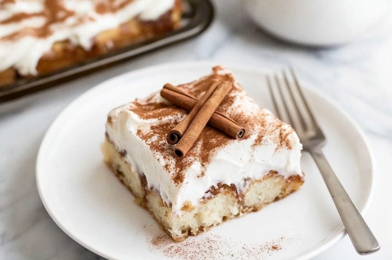 A plate of cinnamon roll poke cake with cream cheese frosting and milk on the side.