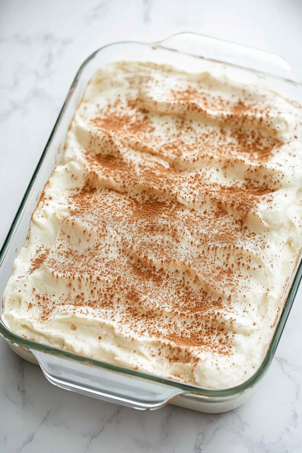 A baking dish filled with cinnamon roll poke cake and topped with cream cheese frosting