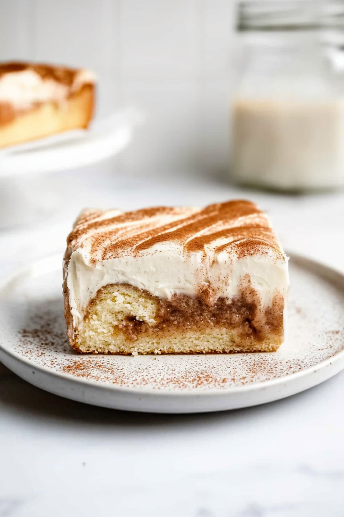 Homemade cinnamon roll poke cake on a plate, served with a glass of milk.