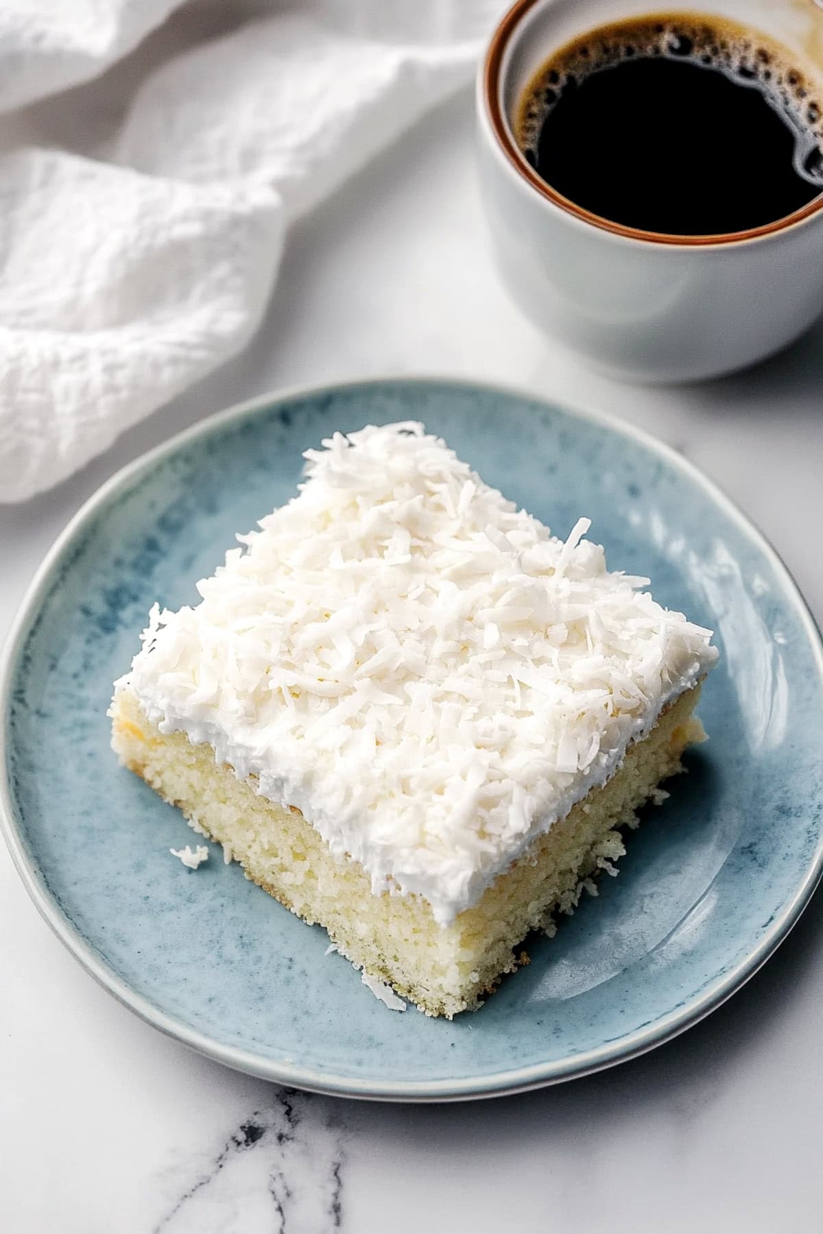 Homemade coconut poke cake served with a cup of coffee.