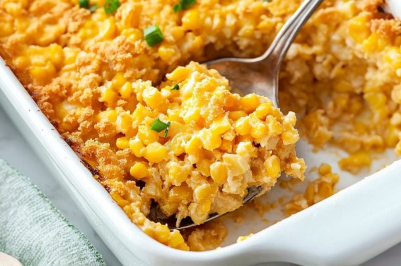 Spoon lifting a serving of creamy corn casserole from baking dish.