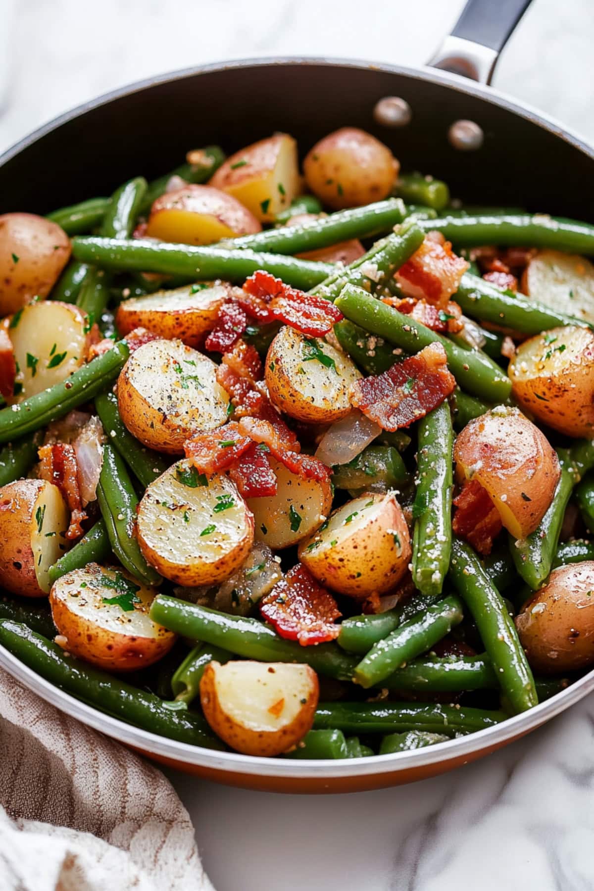 A skillet filled with green beans, red potatoes, crispy bacon and onions.