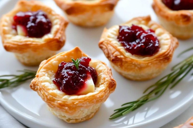 Cranberry brie bites with rosemary sprigs served in a white plate.