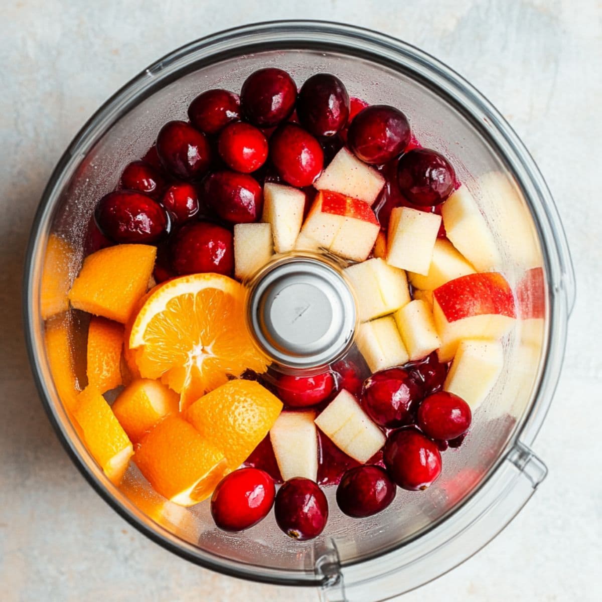 Cranberries, apples and orange chunks inside a food processor pitcher. 