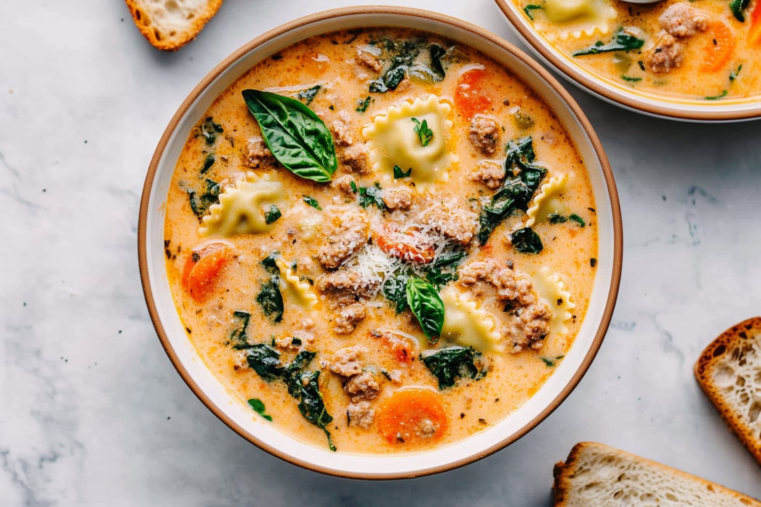 Two bowls of creamy ravioli soup featuring baby spinach, carrots and Italian sausage.