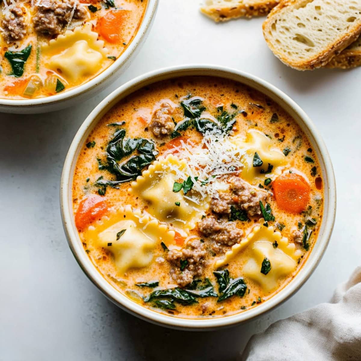 Creamy ravilo soup with vegetables and sausage in a bowl, served with bread.