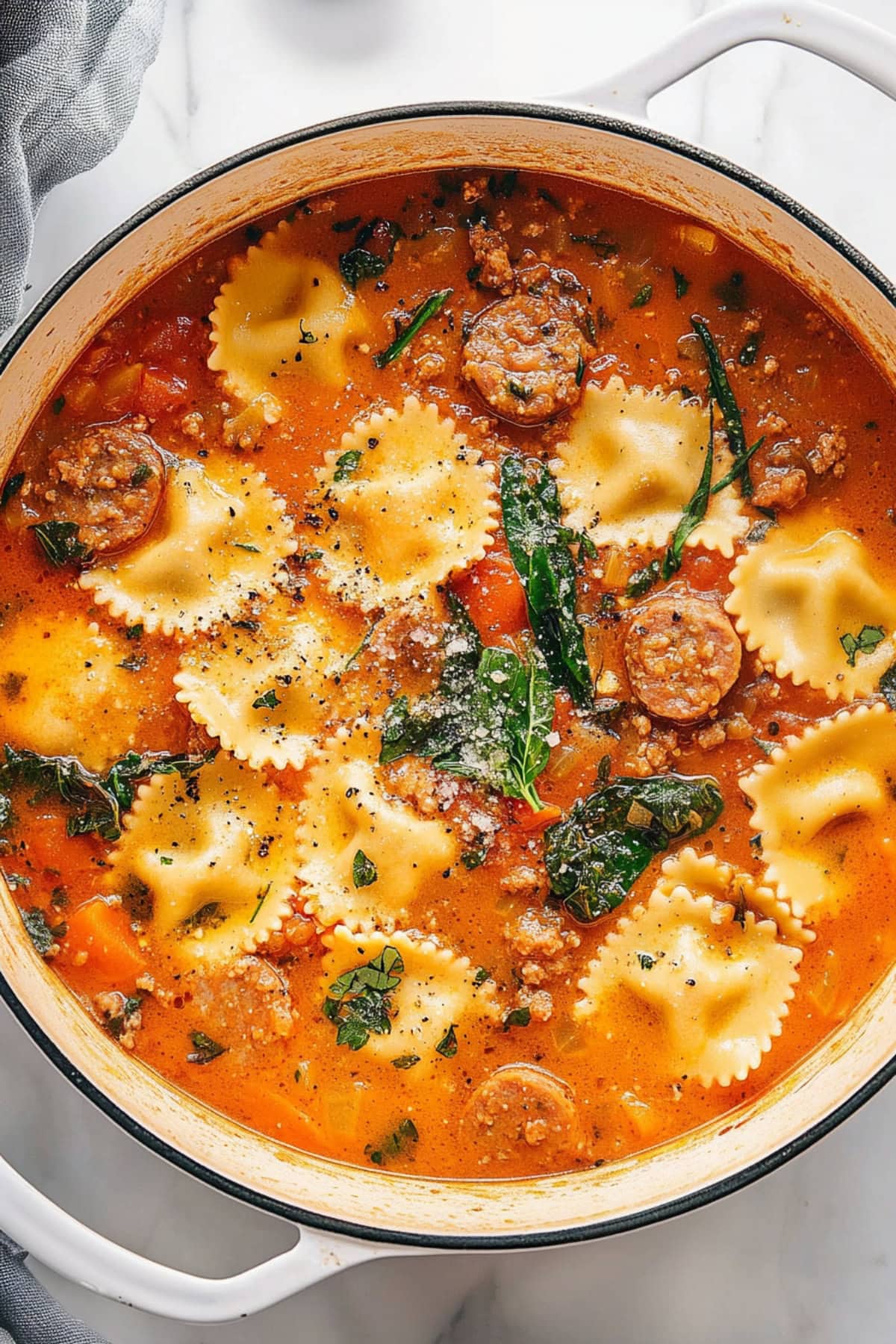 A Dutch oven filled with creamy ravioli soup, with baby spinach, carrots and sausage.