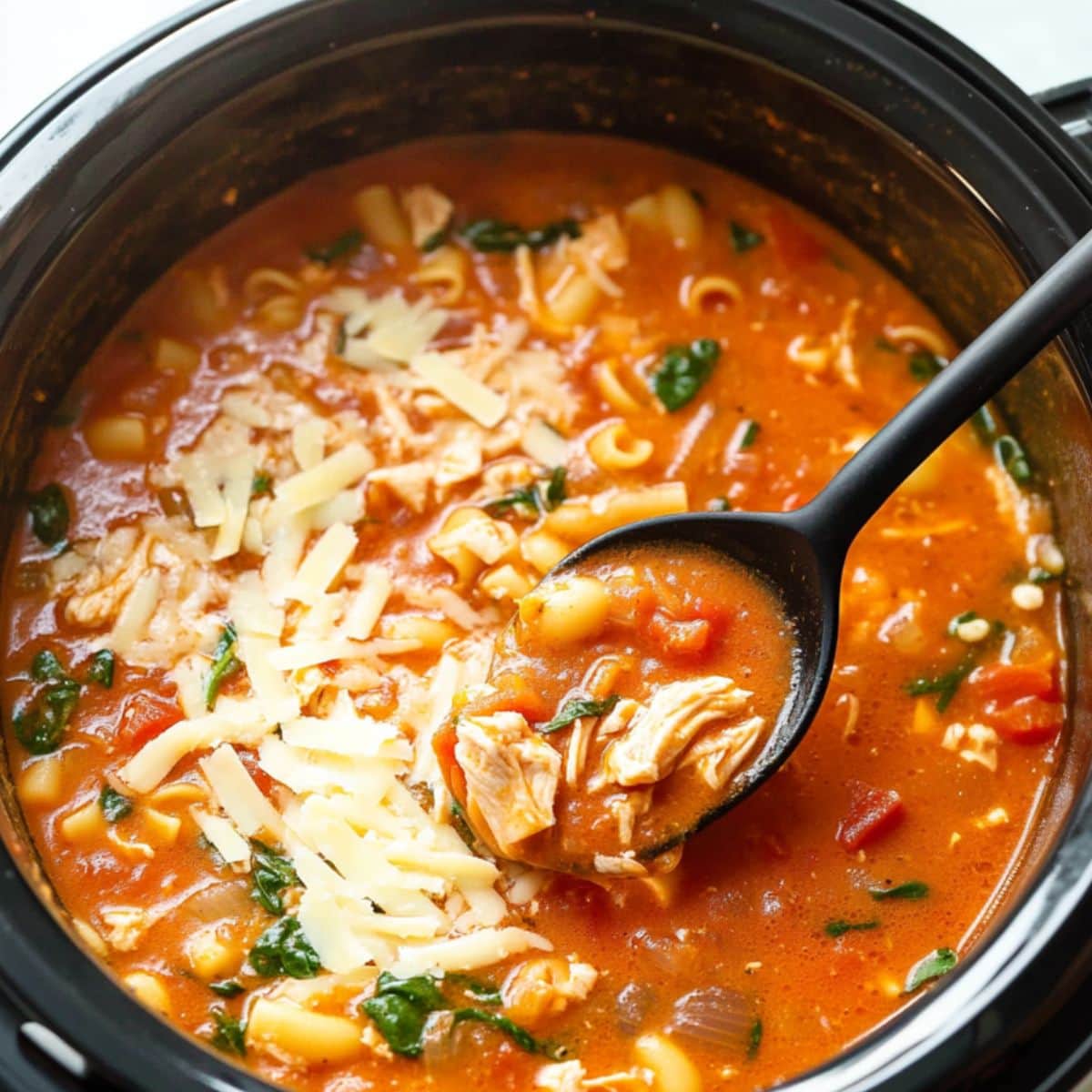 Chicken parmesan soup with shredded cheese cooked in a crockpot.