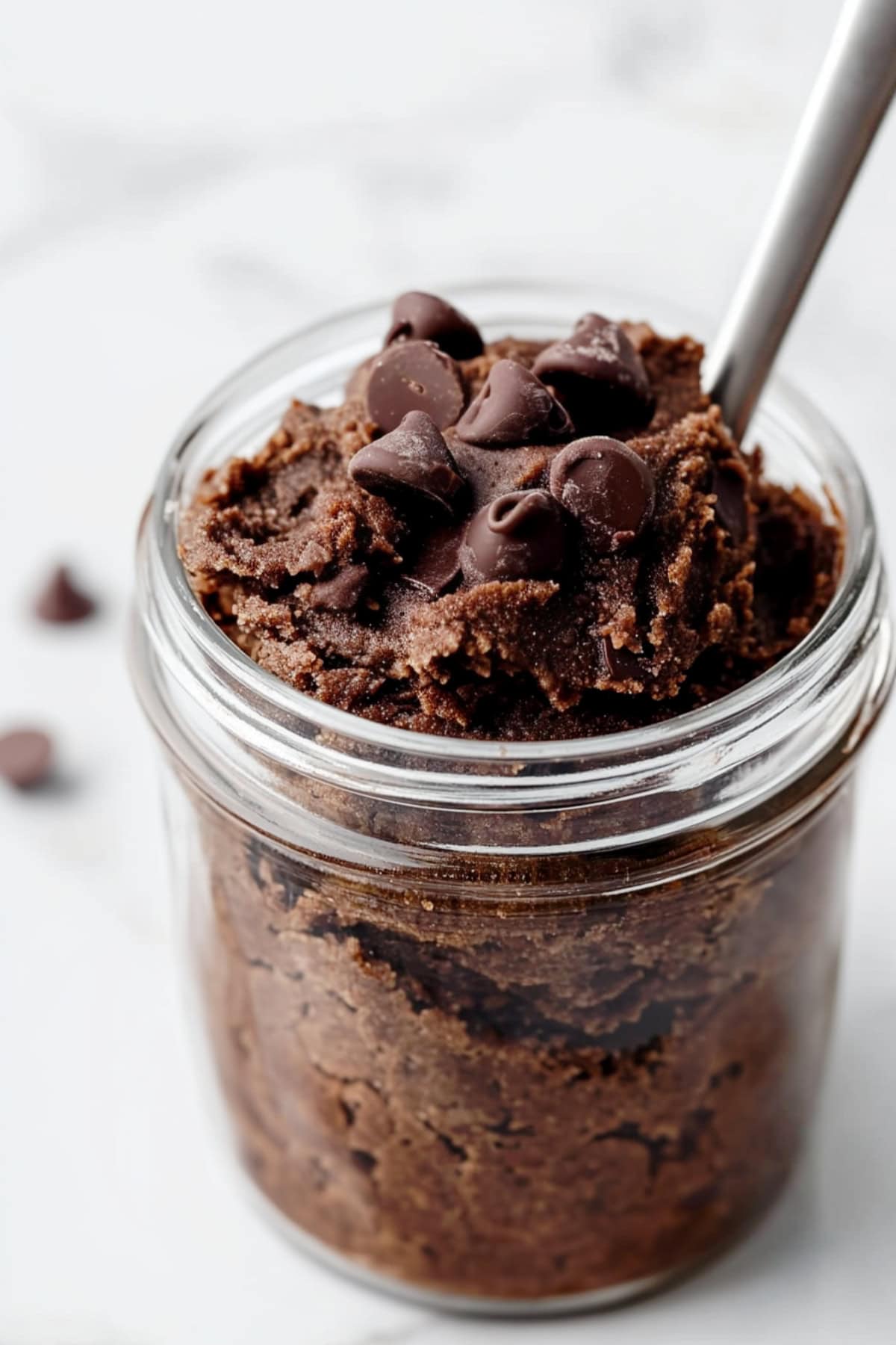 A glass mason jar of rich edible brownie batter with chocolate chips