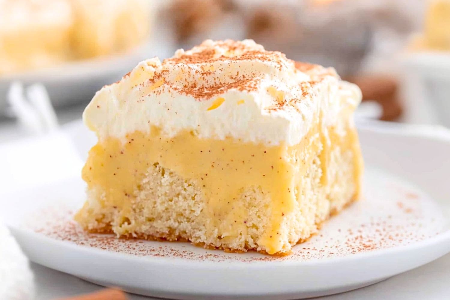 Slice of eggnog poke cake with frosting served in a white plate.