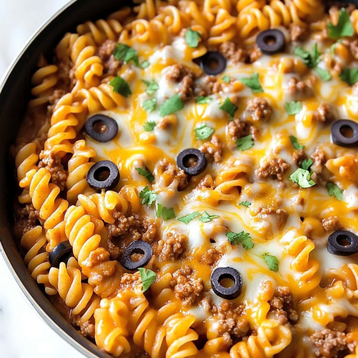 Enchilada pasta with melted cheese cooked in a skillet pan.