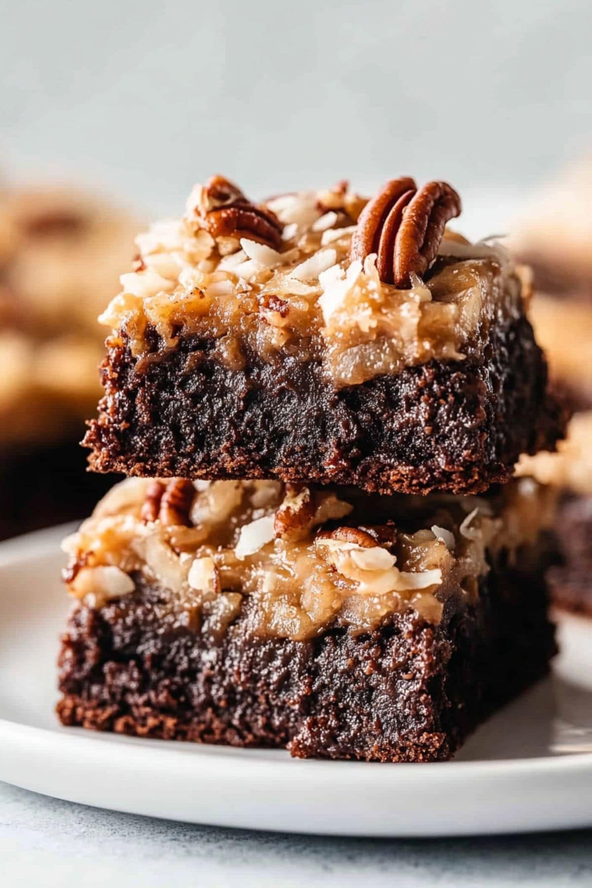 Two slices of German chocolate brownies, with sticky coconut and pecan frosting, stacked on a plate